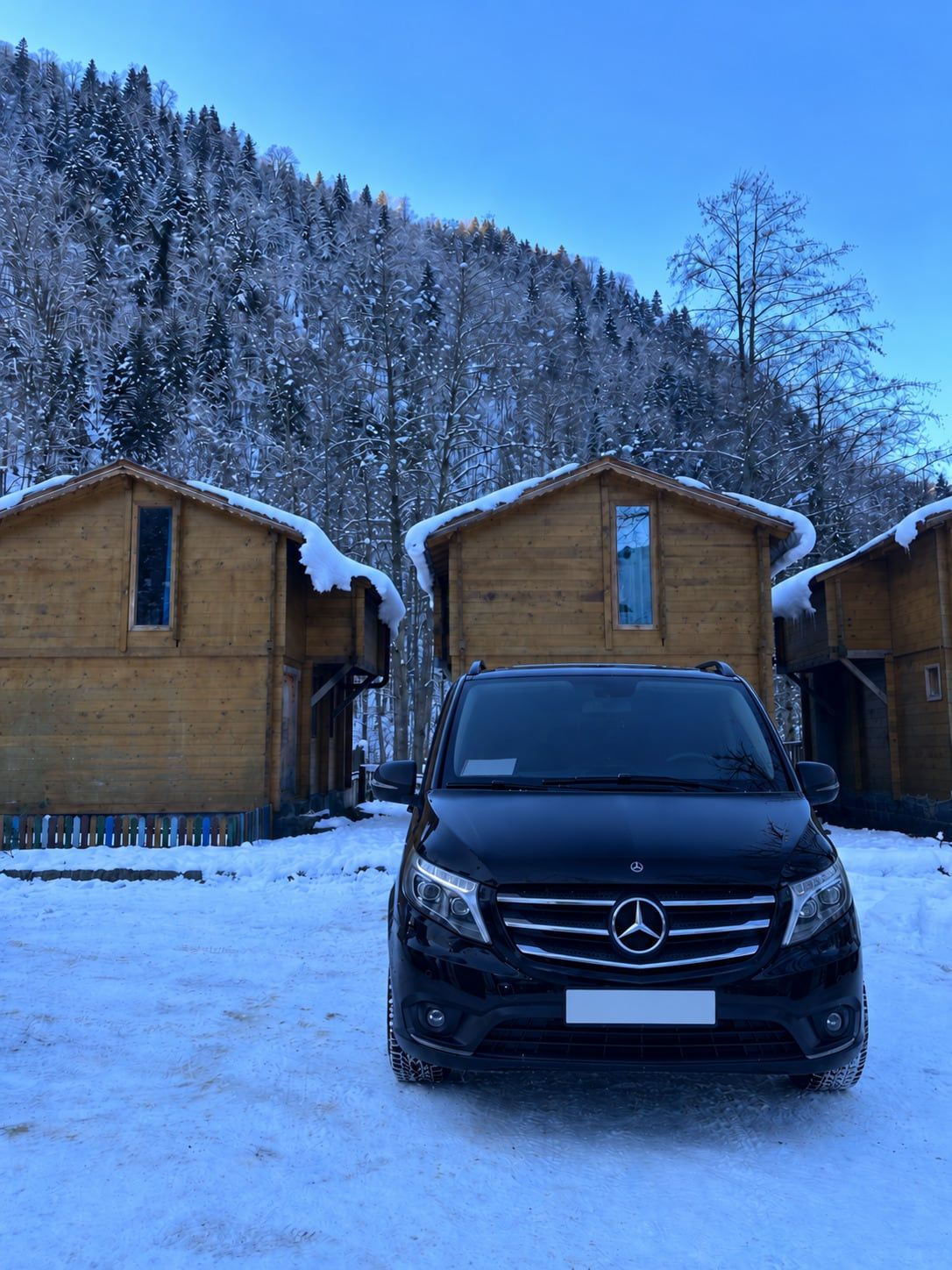 Karla kaplı ahşap bungalovların önünde siyah Mercedes Vito